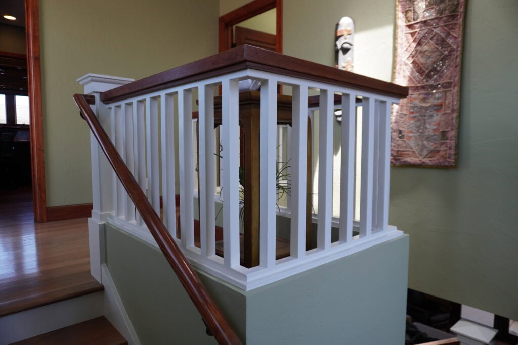 Interior staircase railing painted white with wooden handrail in a home.
