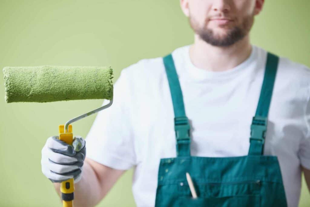 Paint roller with green paint on a wall, professional painting service.